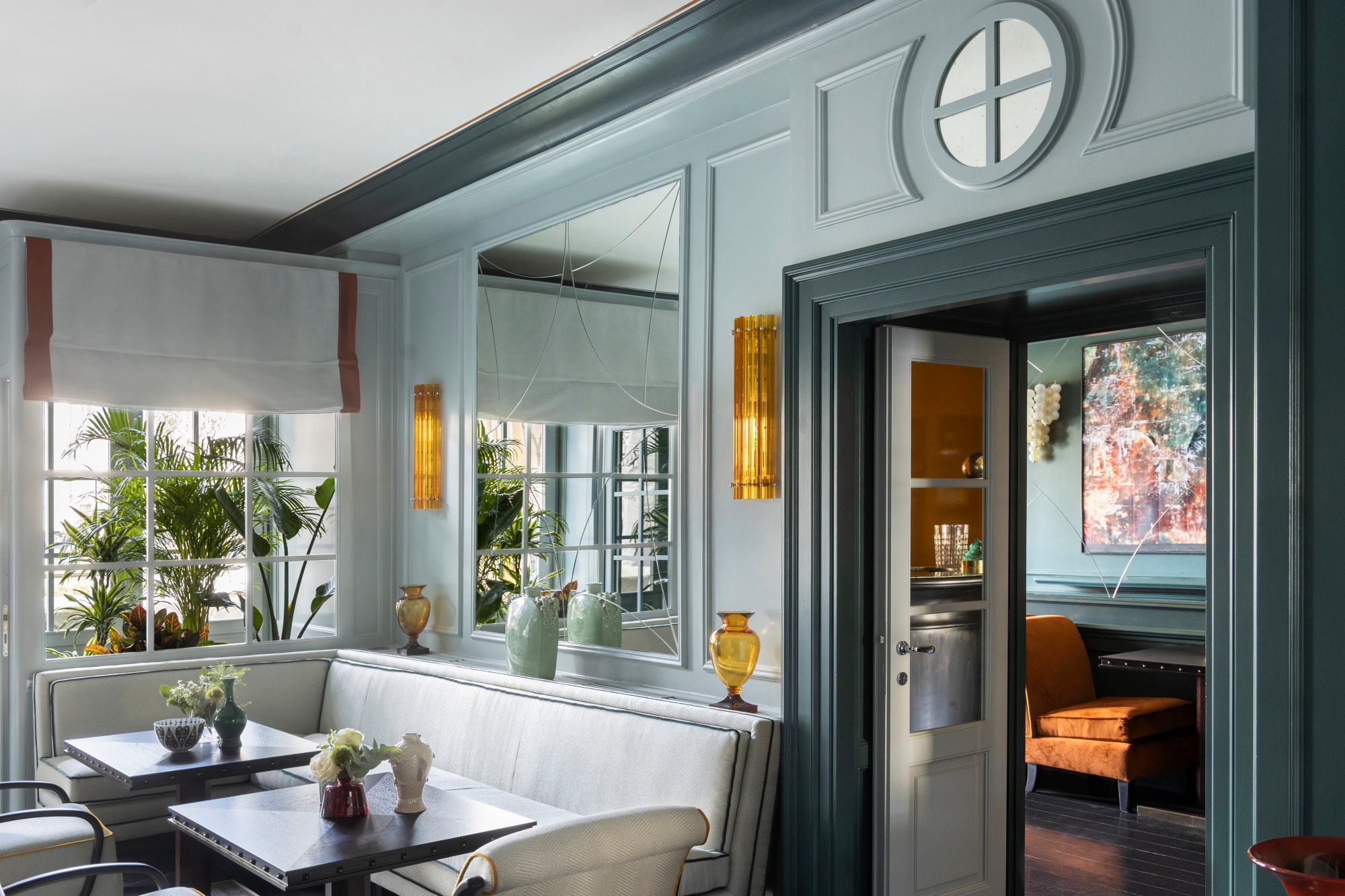 a teal restaurant dining room with a pair of tables holding small vases of white flowers