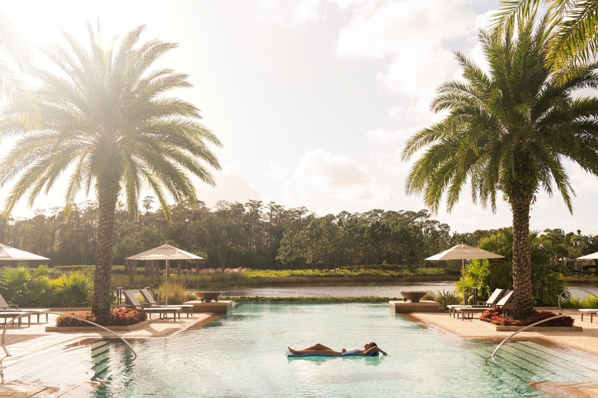 A woman lays on a floating mat in the middle of Four Seasons Resort Orlando's adults-only pool, surrounded by palm trees