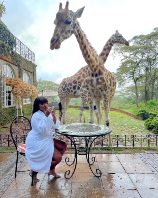 Fora travel agent Valerie Fervil sitting at table with giraffes in the background on a cloudy day