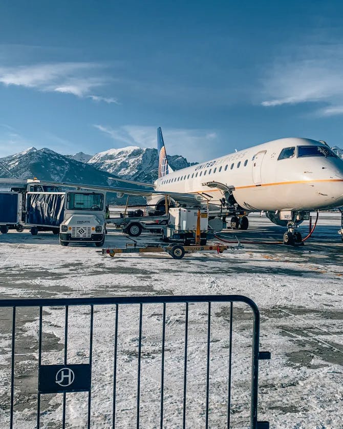 Picture of a plane at the airport with a snowy runway and mountains in the background 