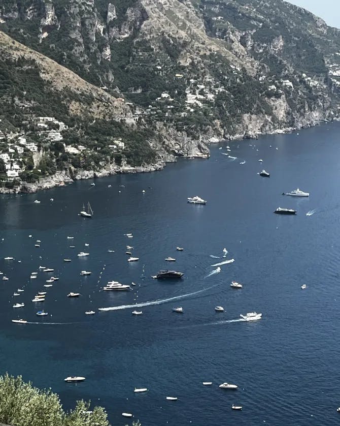 An aerial view of boats sailing on the deep blue sea near a mountainside 