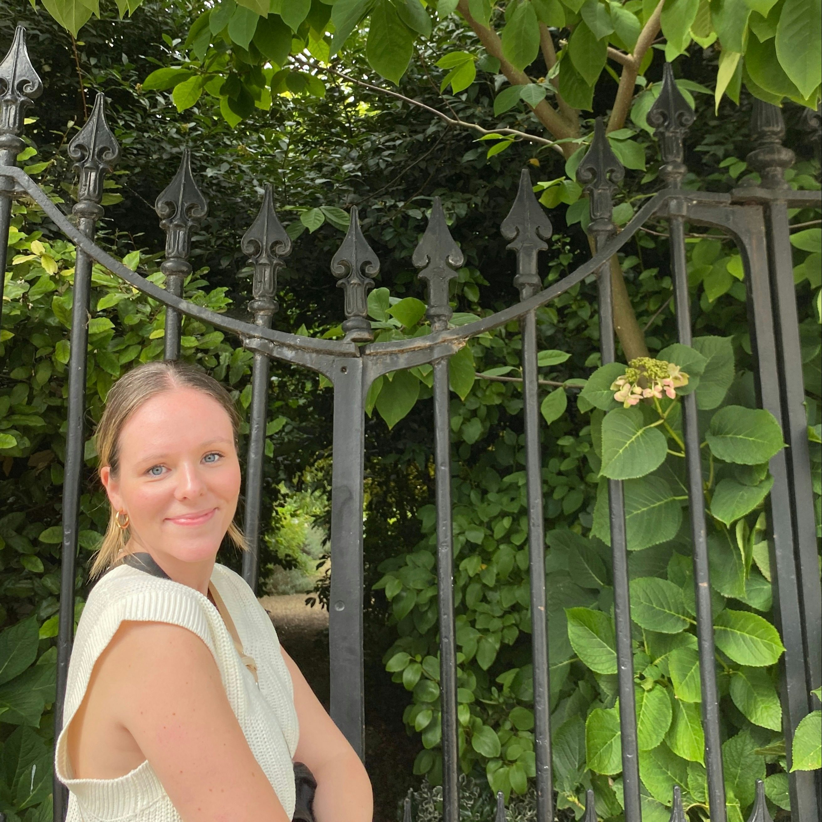 Travel Advisor Maggie Penn in a yellow shirt in front of green plants and an iron gate.