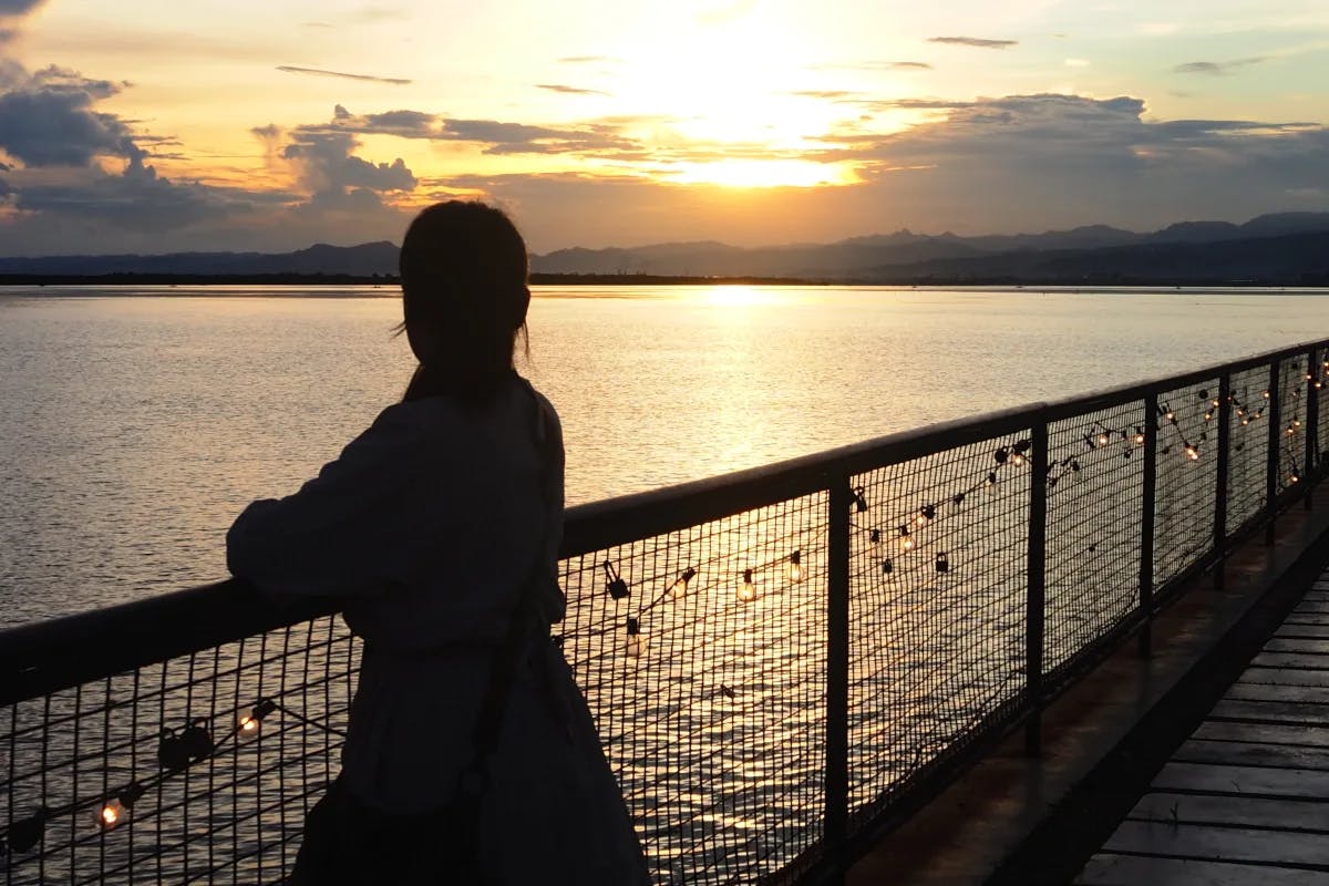 A picture of a girl standing near the railing watching the sunset.