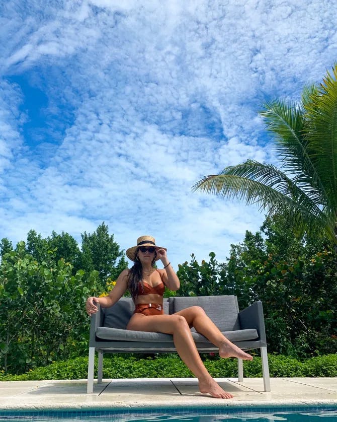 Amanda wearing a bikini while sitting on a chaise lounge by a swimming pool near a palm tree.