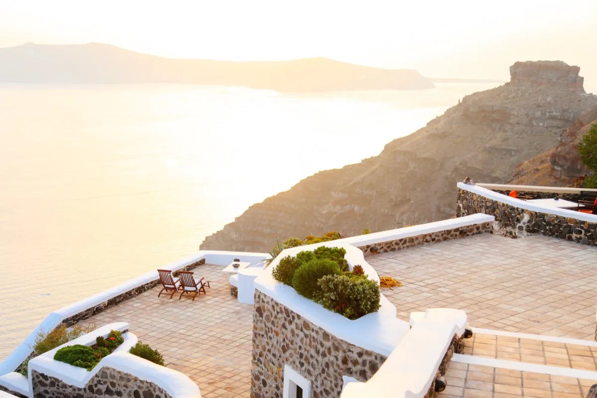 The roof of a Santorini cliffside resort, with cobblestone walls and whitewashed accents. Beyond the resort, the Mediterranean is bathed in a golden sunset