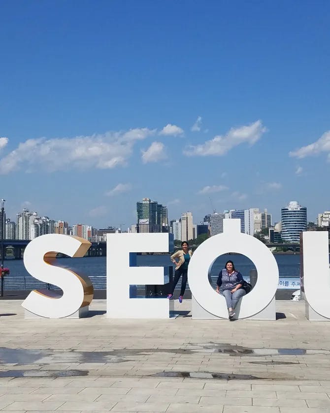 Posing outside with a Seoul sign in front of a city skyline on a sunny day