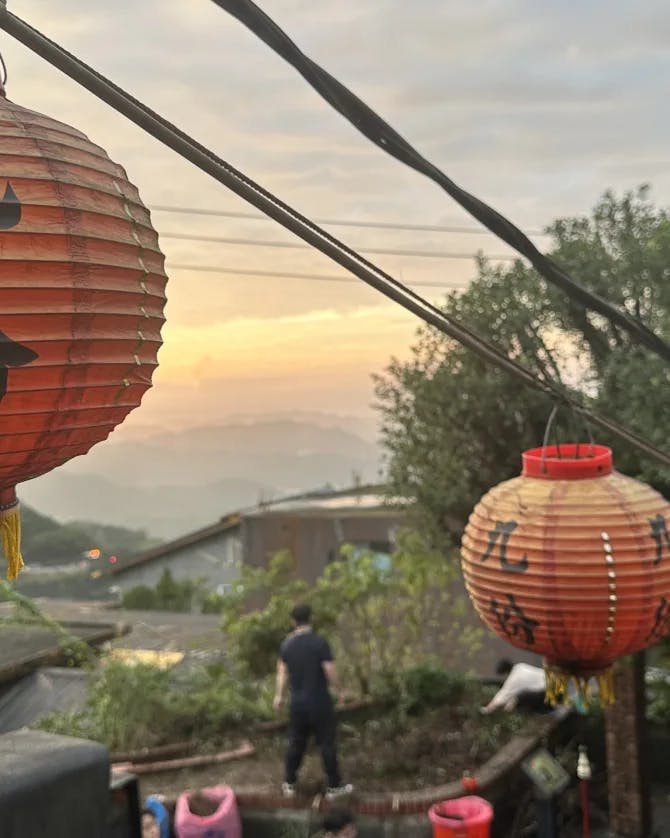 Red Japanese lanterns hung on a line with trees and a sunset in the background