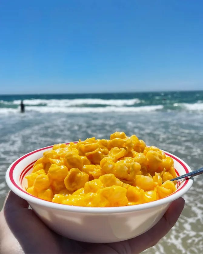 Pasta plated in a white and red bowl with an eating utensil positioned in front of a view of the ocean