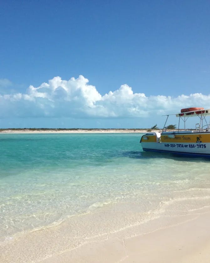 Picture of a yellow and white boat at the shoreline against white sand and crystal blue water