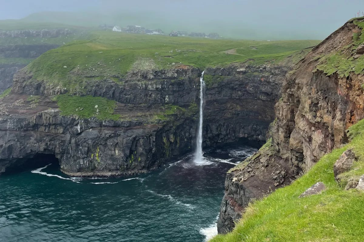 Mulafossur Waterfall majestically cascading from towering cliffs onto the rocky shores of Vágar Island in the Faroe Islands.