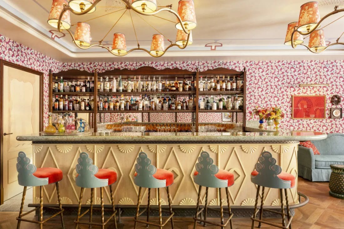 a whimsical colorful bar with blue bar stools. colorful wallpaper, and vibrant light fixtures