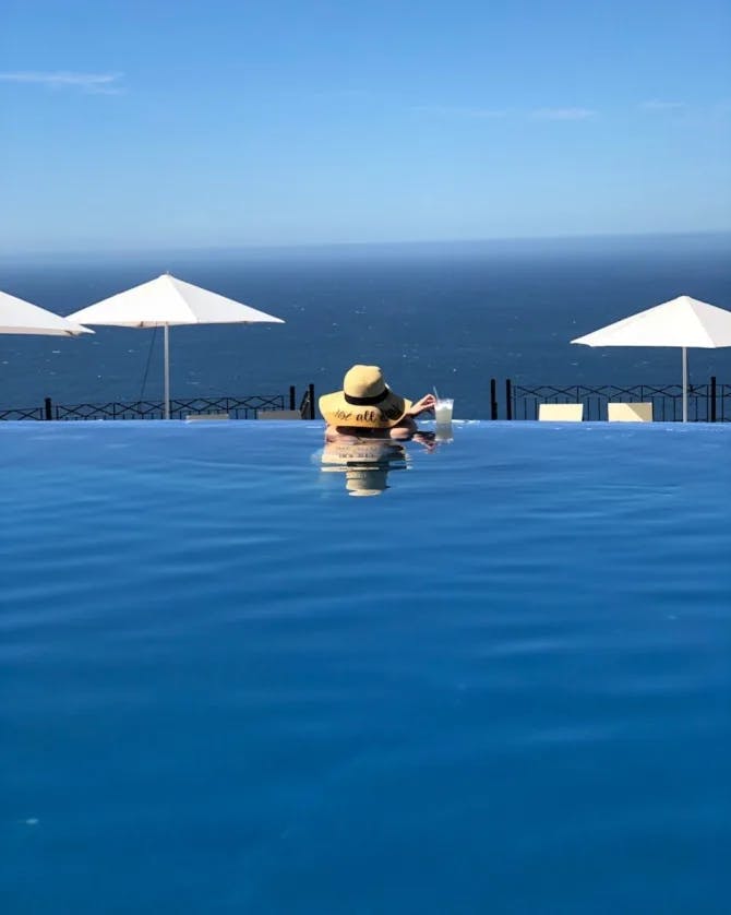 Picture of Nicole in an infinity pool in a sun hat looking over the ocean.