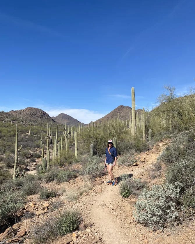 A picture of Anne hiking in the desert with cacti and mountains in the background