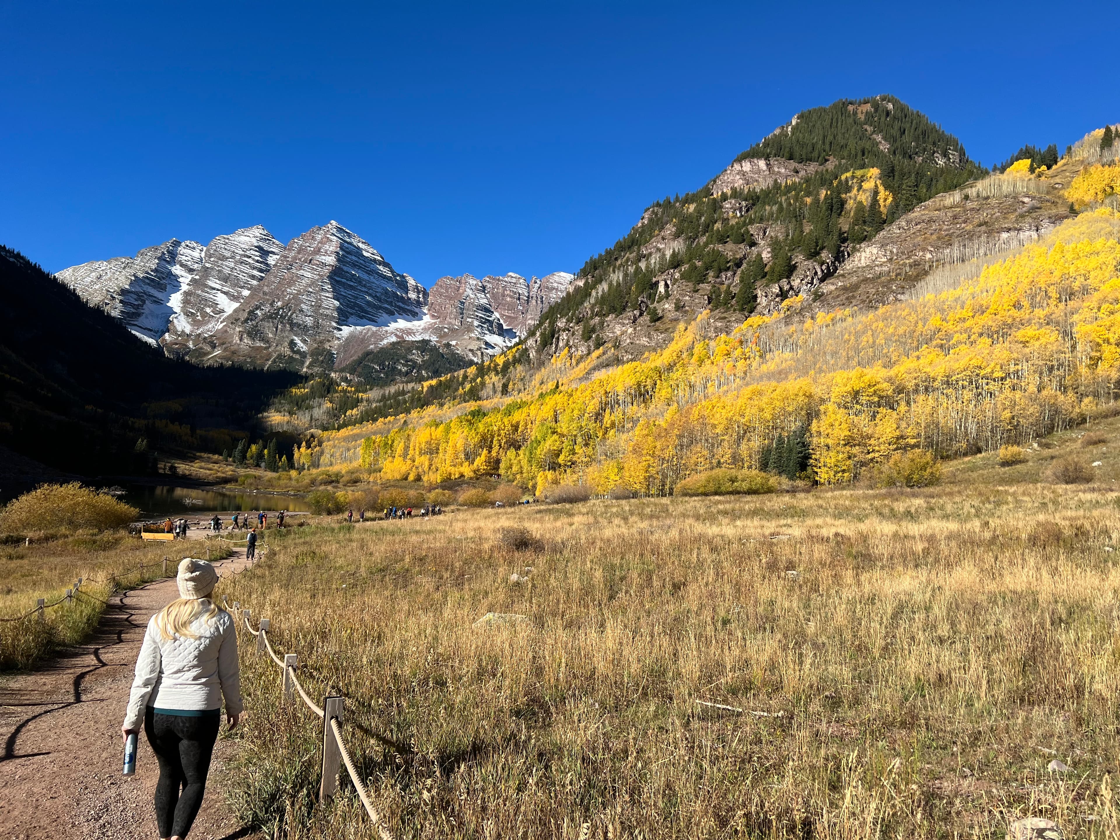 Alexa walking on a dirt path surrounded by wild grass and autumnal trees leading to a mountain