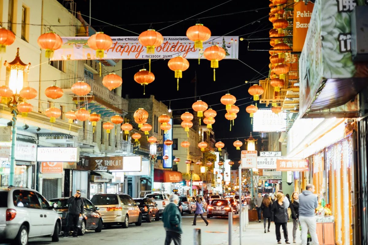 A busy street with Chinese lanterns hung above during the nighttime