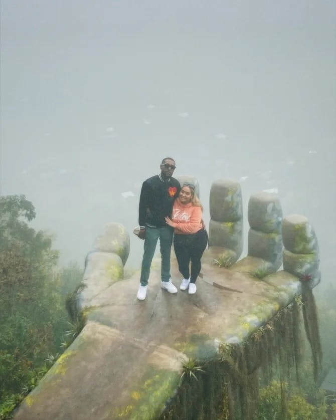 Layne and his partner posing on a stone hand sculpture with fog in the background