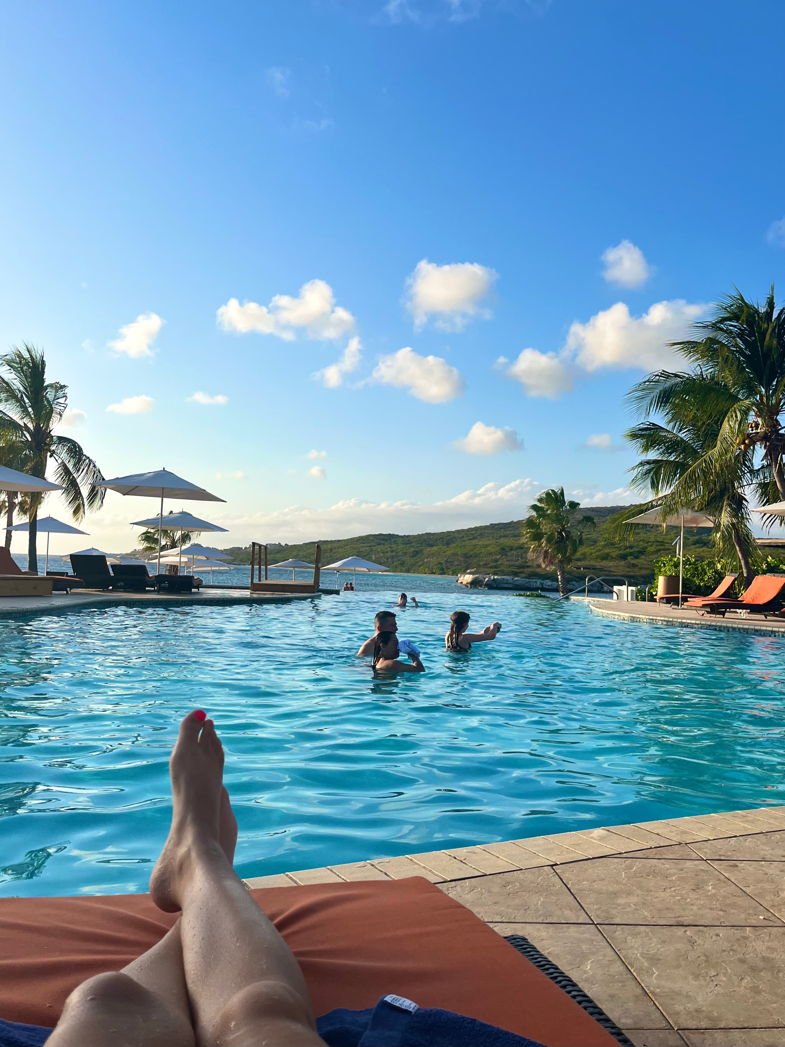 Point of view from a lounge chair looking out towards a pool and the landscape beyond.