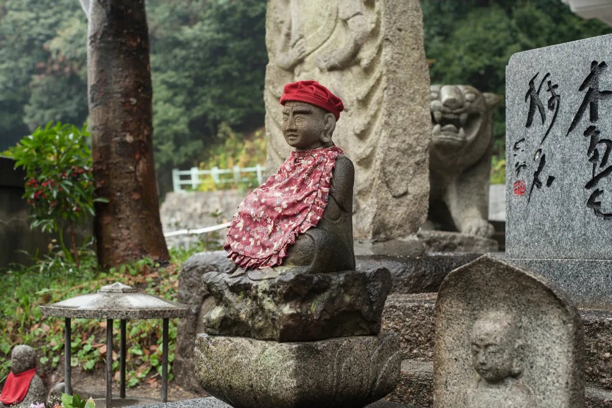A picture of a concrete statue with a red cap and dress, sitting on a bench.