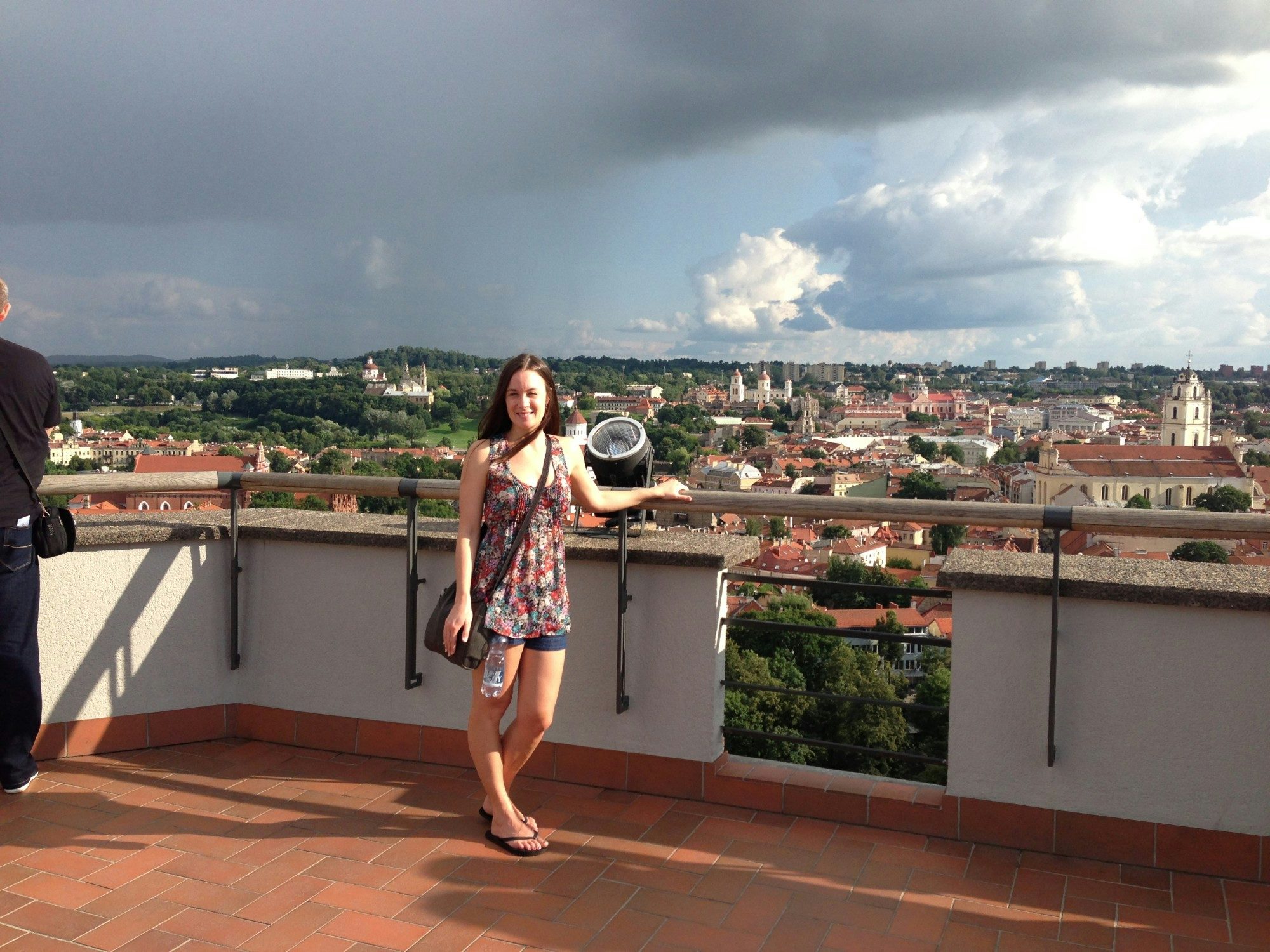 Travel Advisor Jenna Marcinkevicius stands on a roof lookout over a a city with a storm cloud approaching