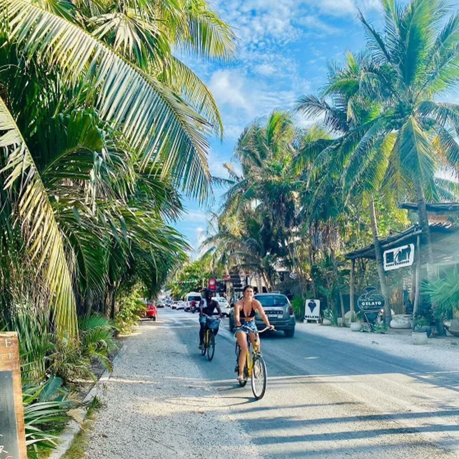 Picture of Heather cycling down a busy road lined with palm trees and houses on both sides