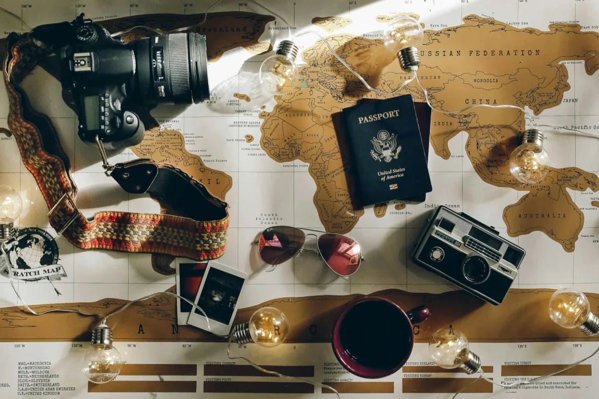 A high-end camera, U.S. passport, trendy sunglasses and other travel-related items are laid out over a vintage map of the world