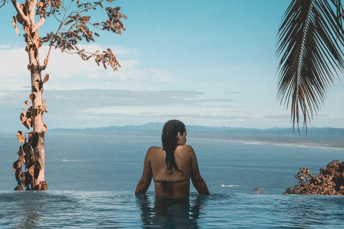 A woman stands at the edge of an infinity pool looking out over a Costa Rica beach