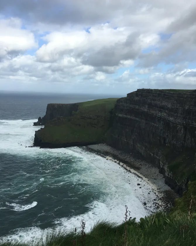 A picture of the dark Cliffs of Moher with crashing waves under a cloudy sky 