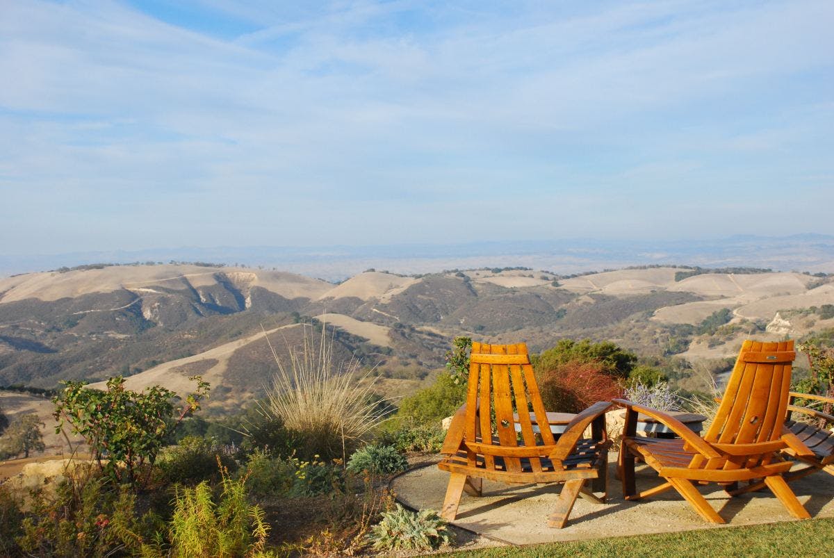 Two wooden chairs looking out onto rolling hills during daytime