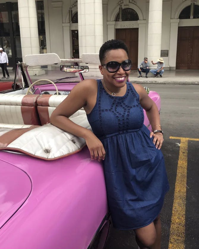 A picture of Kenya posing in a navy blue dress against a hot pink car outside
