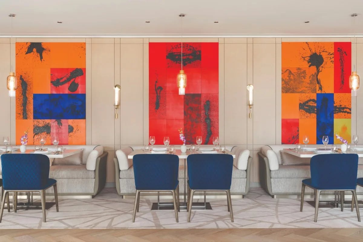restaurant dining room with large red paintings and tables flanked by blue velvet chairs