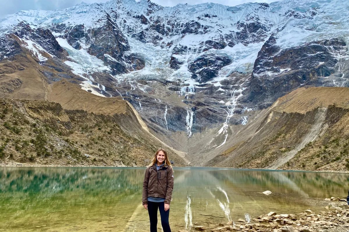 a woman with blonde hair stands in front of a mountain lake
