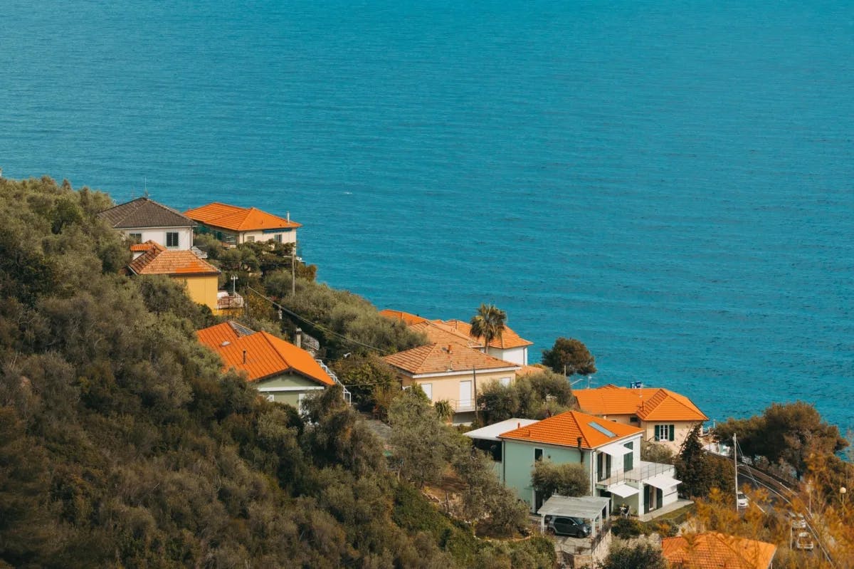 Orange-roof homes stand along a hill on the coast of Cervo, Italy with calm, blue water in the background