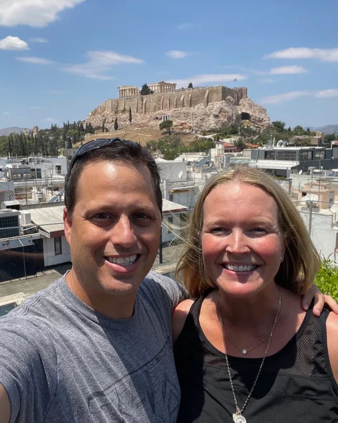 A couple posing for a selfie with a city and Greek temple in the background