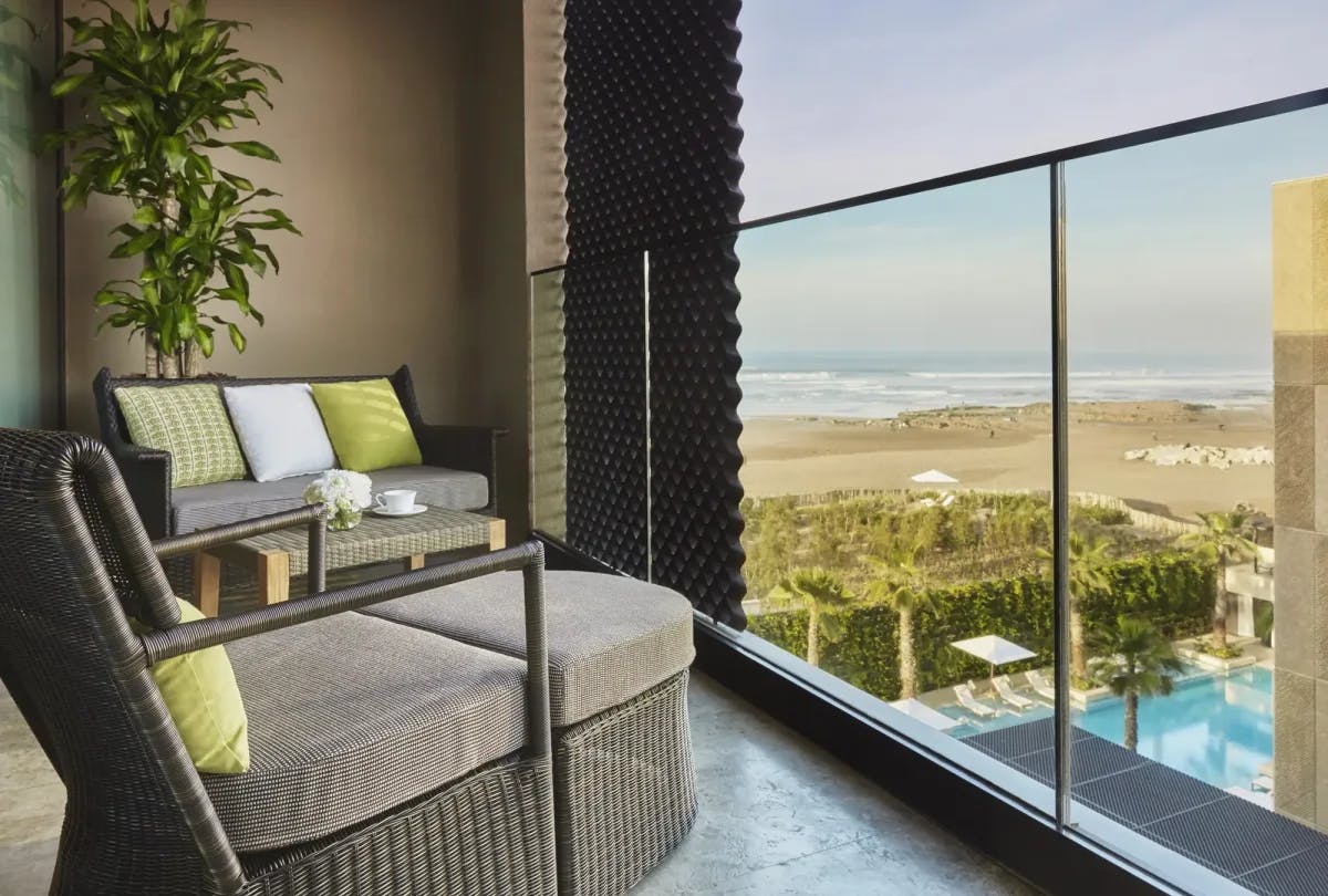 Comfy loungers are positioned toward a glass railing on a private terrace overlooking the hotel pool and beachfront