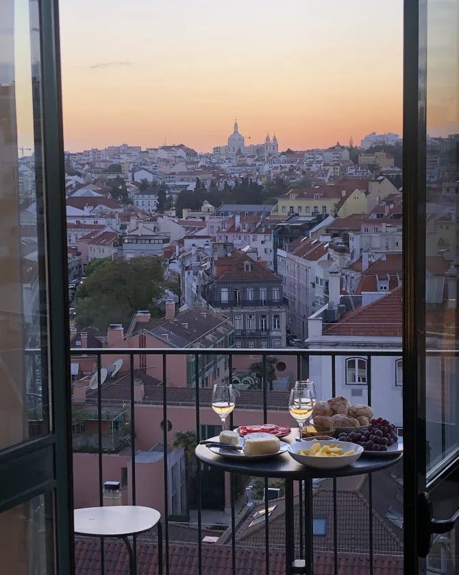 A table with wine glasses and food on a terrace overlooking a city at sunset 
