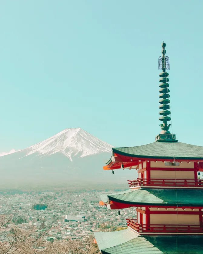 A red-and-white Japanese pagoda overlooking a mountain and a city below.