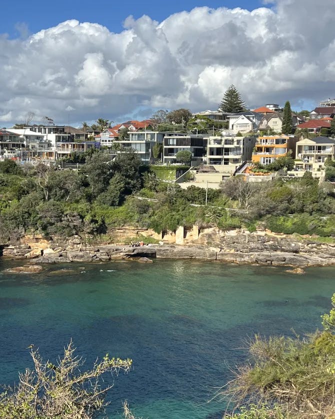 A coastal city view of a rocky shoreline, green trees and blue water 