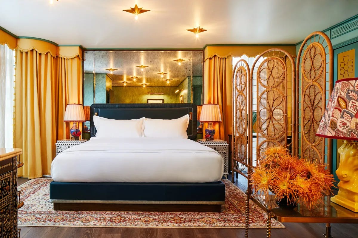 a white bed in a hotel room, with a bright patterned rug and pops of orange