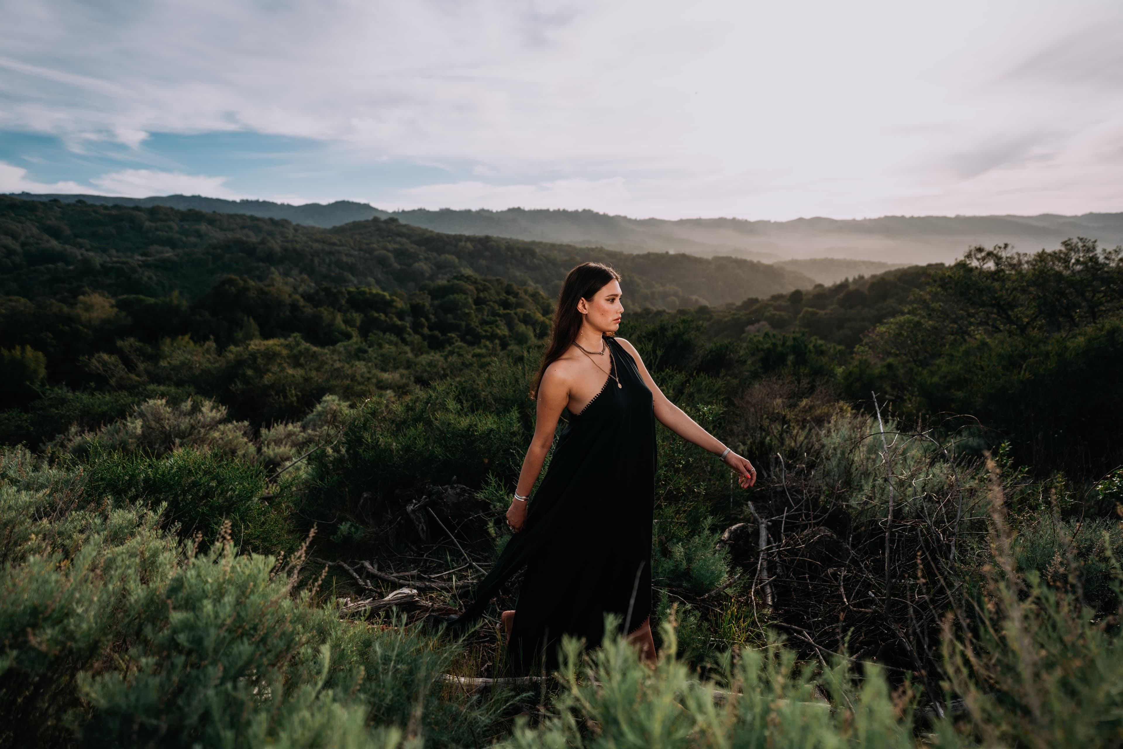 Annemarie wearing a black dress outside surrounded by green trees and shrubs.