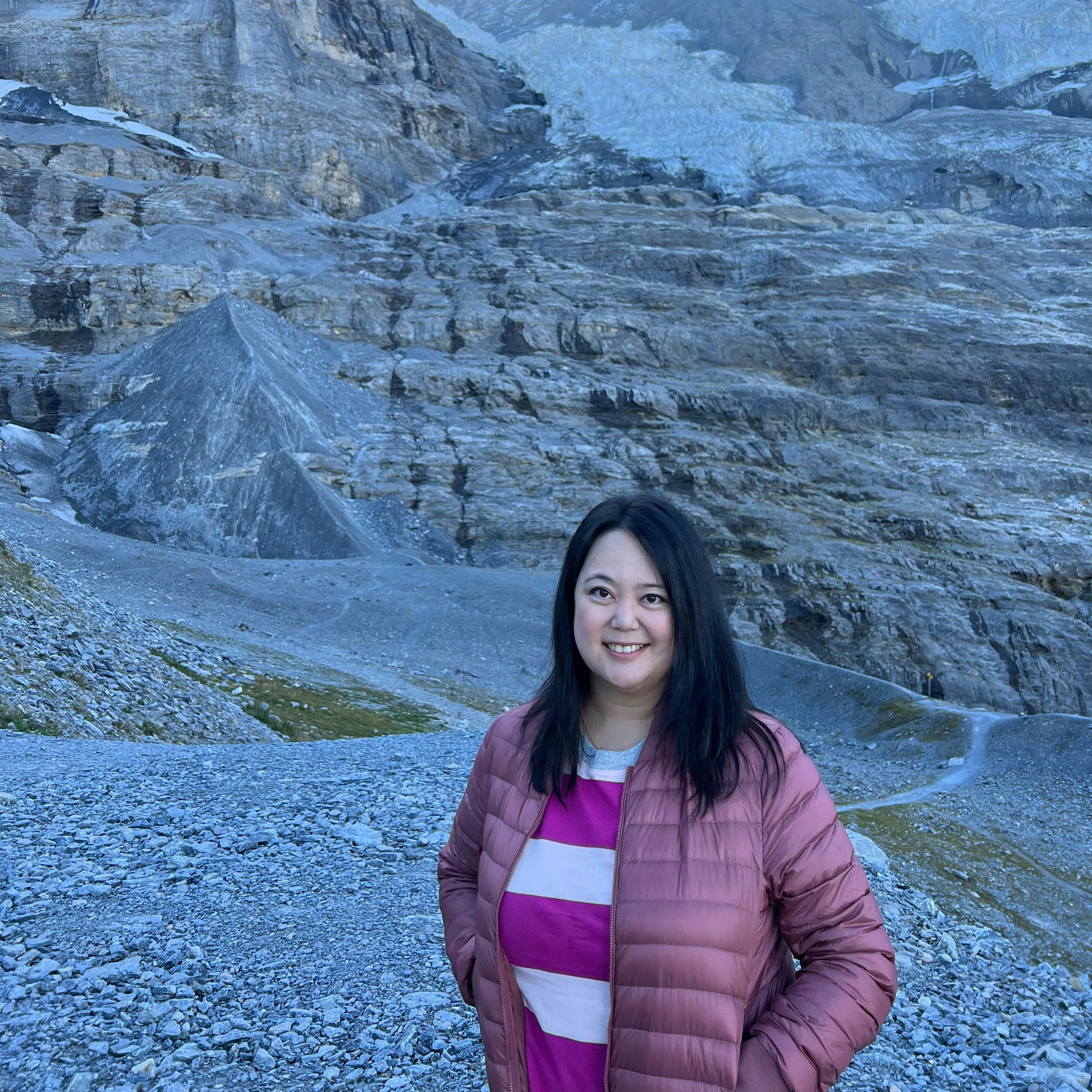 Travel Advisor Jennifer Hoe in a pink puffer jacket with snow-capped mountains in the background.