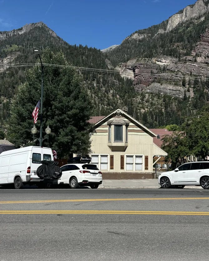 A view of mountains, a house and three white cars from the road.