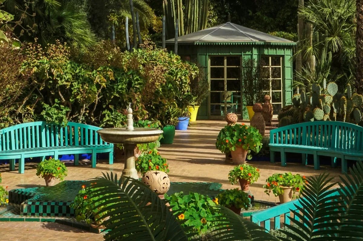 A small courtyard in Jardin Majorelle: turquoise benches are surrounded by a variety of potted plants and lush vegetation
