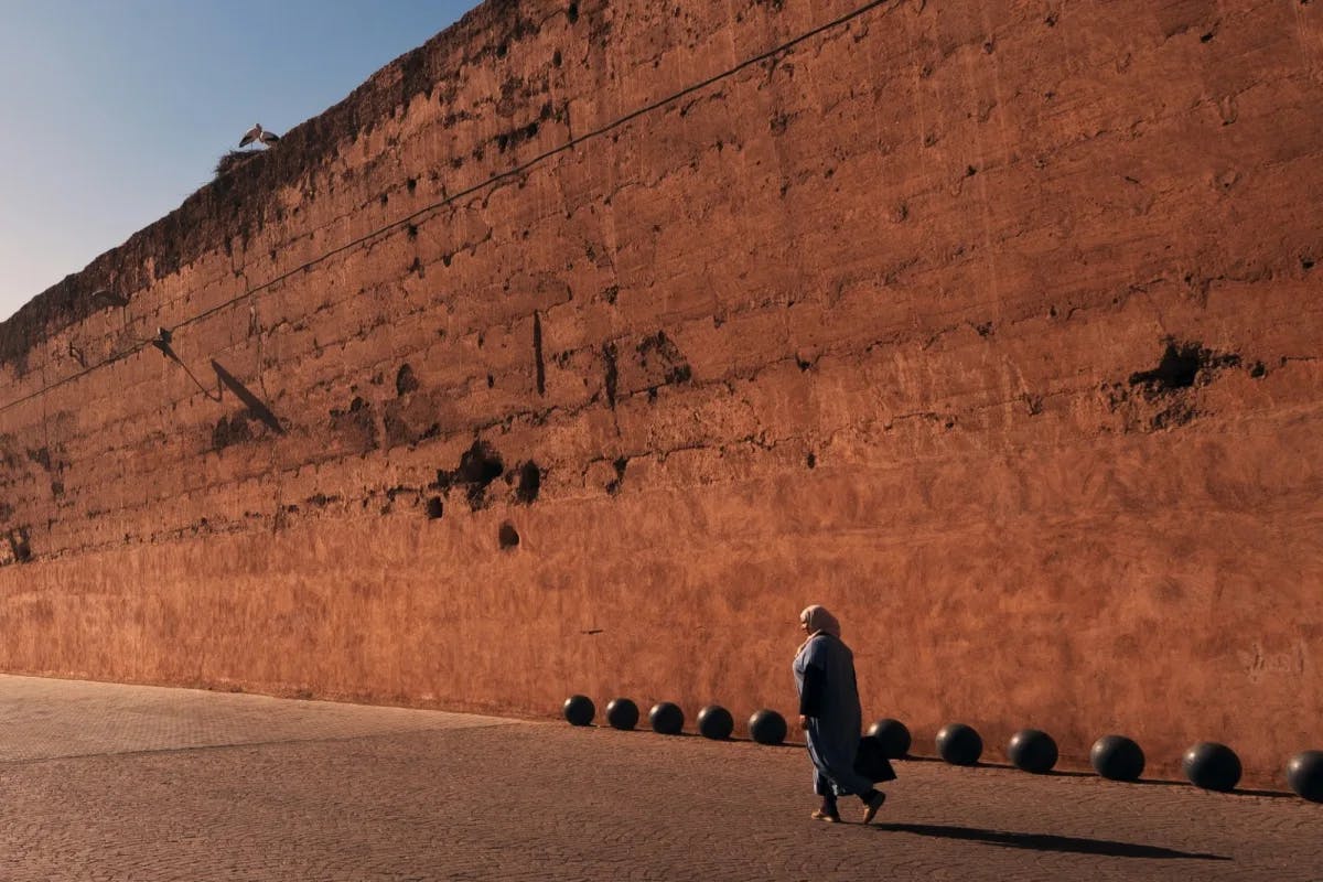 A woman walks along the tall, ancient walls of El Badi Palace near Marrakech