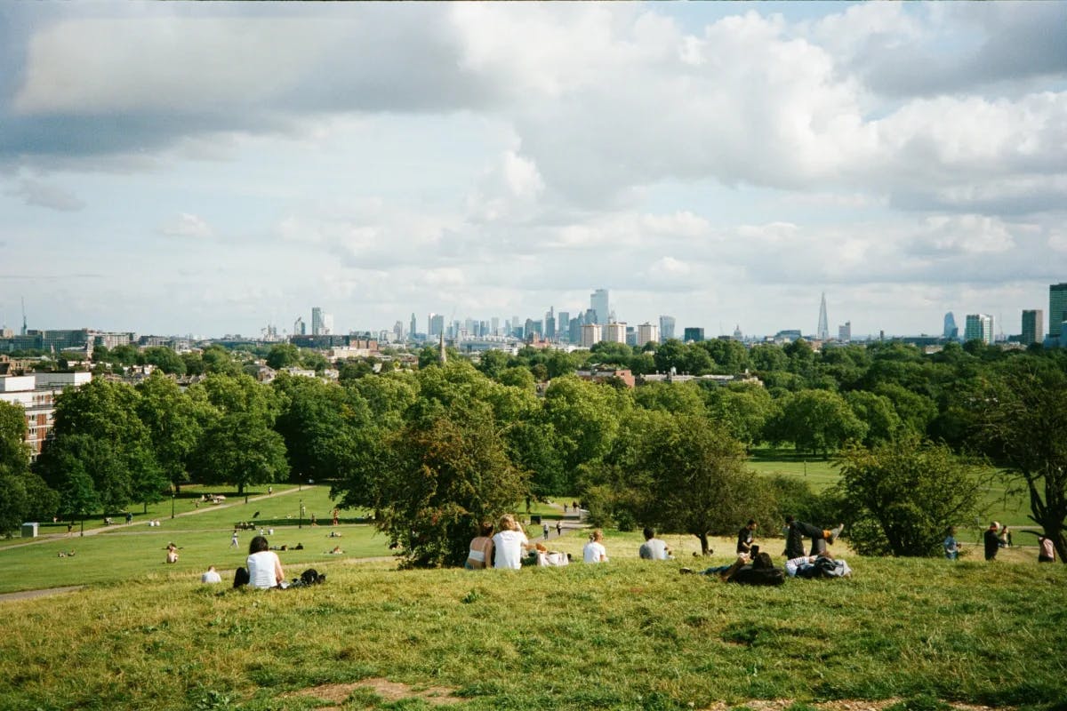 People sit on a grassy hill overlooking an urban landscape in the distance