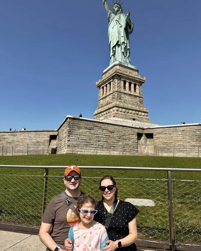 family poses in front of the statue of liberty