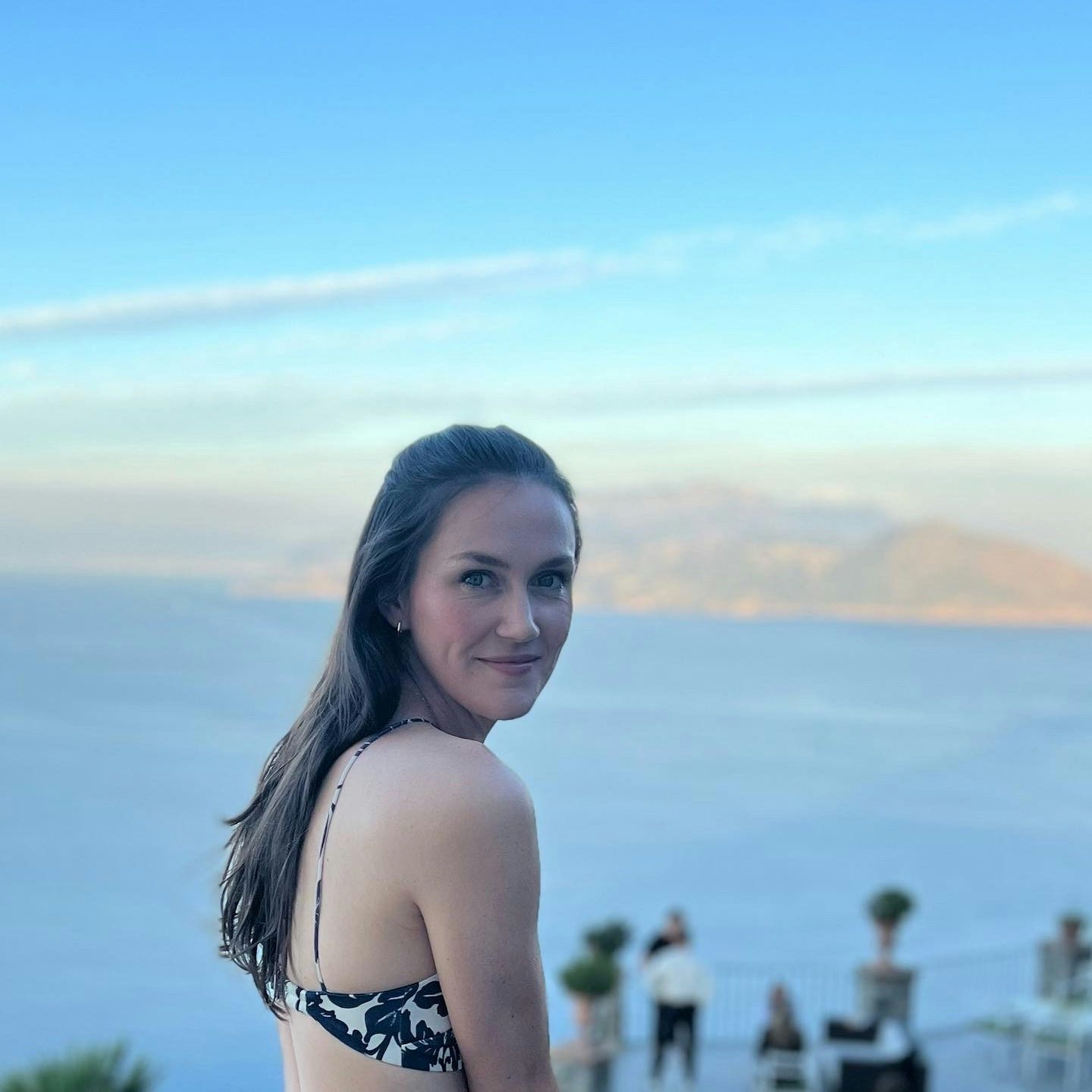 Travel Advisor Grace Hilty wearing a tank top standing in front of blue water and brown mountains.