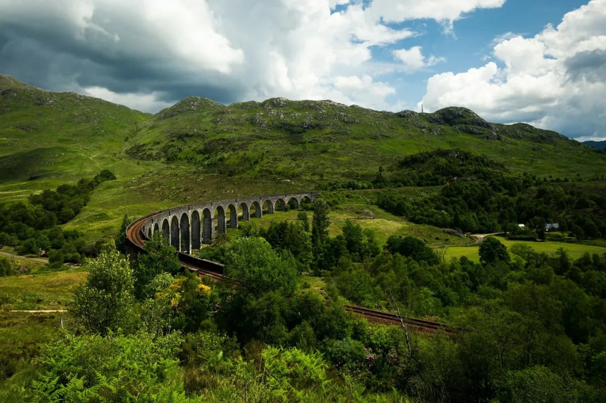 A viaduct runs through verdant Scottish hills with steeper hills occupying the background