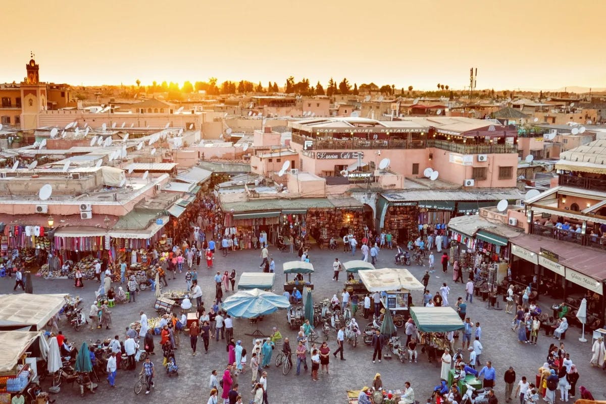 Hundreds of people peruse stalls and shops lining a souk in the Marrakech Medina at sunset