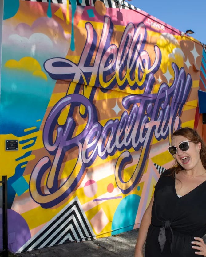 Posing with a wall of graffiti that says 'Hello Beautiful!'