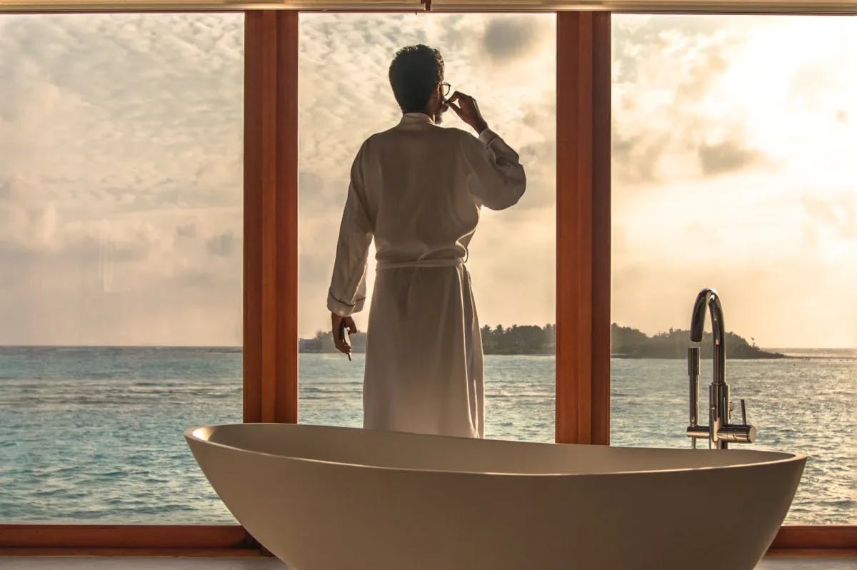 Somewhere in the Maldives, a man in a robe sips a small glass in front of a luxury spa while starring out at the ocean.